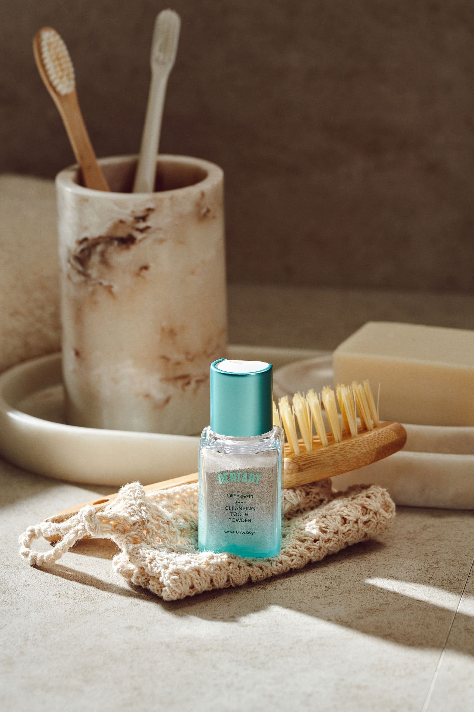 Dentart Deep Cleansing Tooth Powder bottle on a stone bathroom tray beside a bamboo toothbrush and marble brush holder